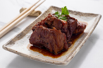 Braised pork spare ribs with soy sauce in Thai Chinese cooking style, served in a rectangular serving plate. This gourmet dish is tender, juicy and delicious to try.