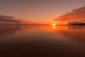 Fototapeta na wymiar Vibrant sunrise in red shades at a tropical beach, soft waves.