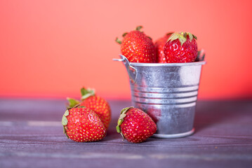 A bucket of strawberries on a dark and red background.
