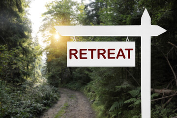 Wooden sign with word Retreat and picturesque view of beautiful forest with path