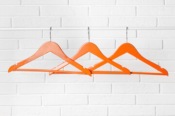 Orange clothes hangers on rail near white brick wall