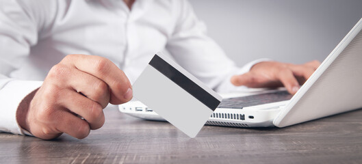 Businessman using laptop computer and holding credit card.