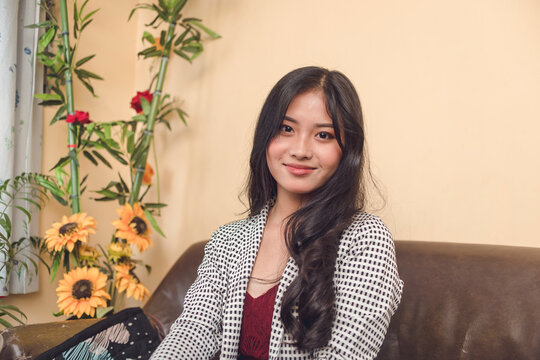 A pretty young professional looking at the camera while sitting at the couch. Late teens and early 20s woman in business attire.