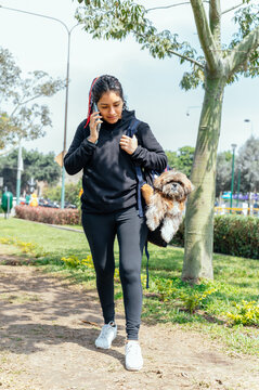 Young smiling woman carrying her dog in a backpack while talking on the phone, outdoor in nature