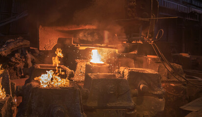 Steel pouring from casting ladle into metal molds.