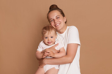 Horizontal shot of smiling satrisfied woman wearing white casual style T-shirt embracing little...