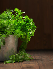 a bunch of green dill and parsley in an iron bucket, dark wooden background, concept of fresh vegetables and healthy food