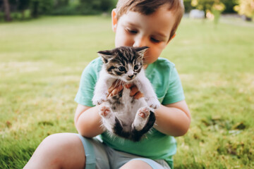 Little kid sitting on grass with kitten in his hands