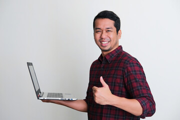 Side view of Adult Asian man smiling confident and give thumb up while holding a laptop computer