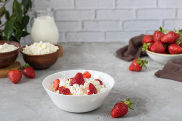 A bowl of cottage cheese garnished with strawberries. Behind her cottage cheese, sour cream, milk.