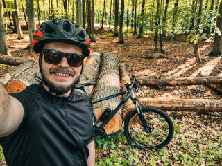 Selfie of a cyclist in the forest wearing helmet and sunglasses. Man smiling while riding his...