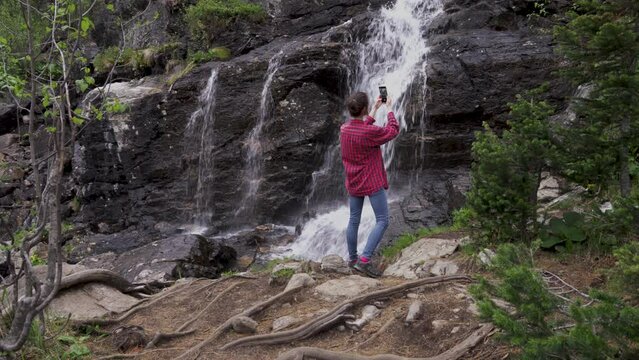 Young girl tourist with phone takes pictures of waterfall in forest