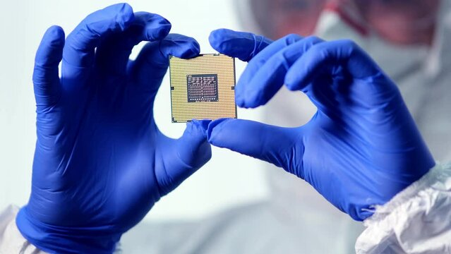 A young computer engineer holds and tests a processor. Close-up of a male engineer holding a microchip with gloves and examining it - a state-of-the-art electronics manufacturing plant