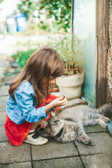 Little girl playing with a grey cat outside