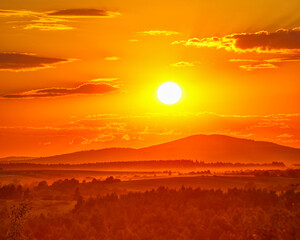 The setting sun in the sky over the wooded hills © SerPhoto