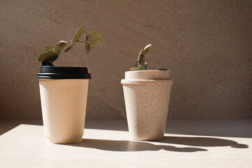 Disposable and reusable eco cups on a stone beige background with eucalyptus branches. Front view