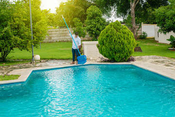 Man cleaning a swimming pool with skimmer, maintenance person cleaning a swimming pool with...