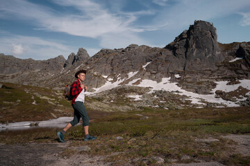 Obraz premium Young traveler tourist dressed as hipster with backpack walks in mountains