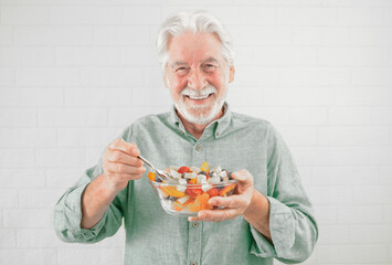 Happy caucasian senior man holding a glass bowl with fresh summer fruit salad, ready to eat