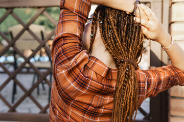 a girl with a dreadlocked hairstyle poses in summer outdoor, bright sunlight, dressed in a plaid...