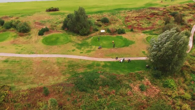 Drone outdoor shot of a group of people standing near a dirt road on a golf course, having fun playing the game in a peaceful scenery. High quality 4k footage