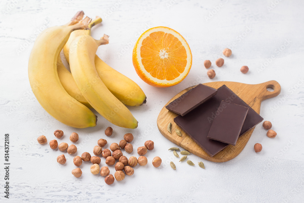 Wall mural Bananas, orange, chocolate, nuts and cardamom on a light blue background. Ingredients for a vegan dessert. Delicious homemade food