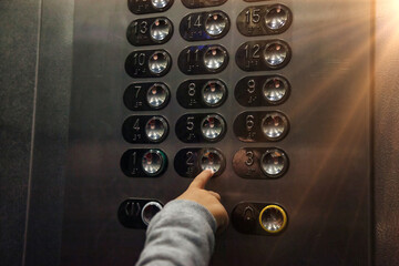 Close-up hand of little child pressing button of number two floor in modern elevator