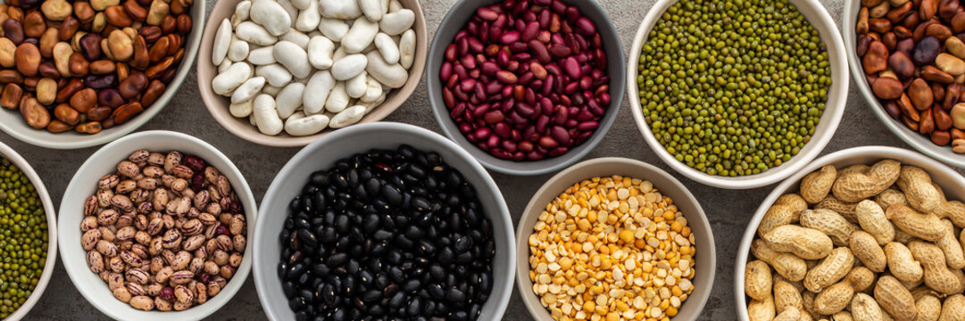 Banner of different types of legumes in bowls, green with yellow peas and mung beans, chickpeas and peanuts, colored beans and lentils, top view