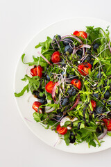 Light salad with arugula and berries, strawberries and blueberries, delicious healthy summer salad on a white background