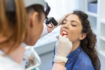 Female patient opening her mouth for the doctor to look in her throat. Otolaryngologist examines...