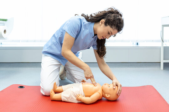 Woman performing CPR on baby training doll with one hand compression. First Aid Training - Cardiopulmonary resuscitation. First aid course on cpr dummy.