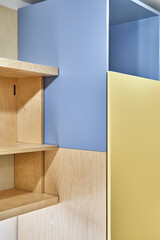 Fragment of plywood book shelves and yellow-blue plywood cabinet at home. Modern domestic furniture...