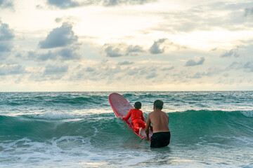 Happy Asian family grandfather teaching grandchild boy surfing on surfboard in the sea on summer...