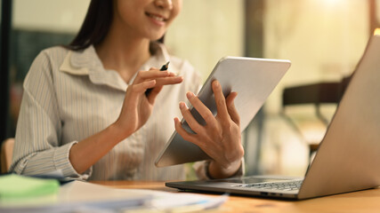 Smiling asian female employee surfing information or checking email on digital tablet