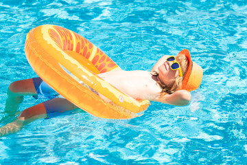Kid boy in swimming pool on inflatable ring. Children swim with orange float. Water toy, healthy...