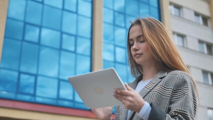 A young girl student works with a white tablet in the city.