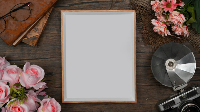 Empty picture frame, retro camera, books and pink roses on wooden background
