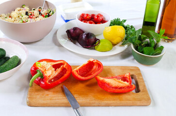 Red pepper on a wooden cutting board. The process of preparing Orzo salad with ingredients on the table. The concept of vegetarian food. Horizontal orientation.
