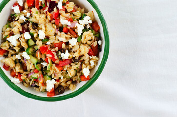 Traditional multi-colored Orzo salad on the table. Tomatoes, cucumbers, feta cheese, olives, red onions, sweet peppers and risoni pasta. Healthy food concept. Horizontal orientation. copy space. Top v