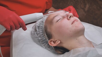 A beautician makes a darsonvalization of the face of a young girl with problem skin.