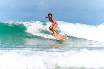 Asian woman surfer surfing and riding surfboard  the wave in the sea at tropical beach in sunny day. Healthy female enjoy outdoor activity lifestyle and water sport exercise surfing on summer vacation