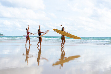 Group of Asian woman surfer in swimwear holding surfboard walking together on tropical beach at summer sunset. Female friends enjoy outdoor activity lifestyle water sport surfing on travel vacation - obrazy, fototapety, plakaty