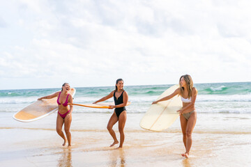 Group of Asian woman surfer in swimwear holding surfboard walking together on tropical beach at summer sunset. Female friends enjoy outdoor activity lifestyle water sport surfing on travel vacation