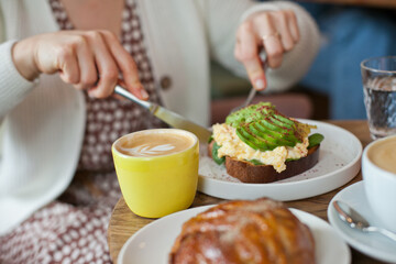 Avocado toast closeup. Young woman at brunch eating and drinking coffee and avocado toast,...