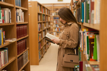 Young woman at the library holding book. millennial reading books, standing between bookshelves in the bookstore. Studying at university library. College or higher education lifestyle concept.