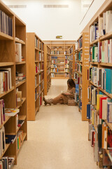 Young woman sitting at the library holding book. millennial reading books, standing between bookshelves in the bookstore. Studying at university library. College or higher education lifestyle concept. © Dina