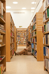 Young woman sitting at the library holding book. millennial reading books, standing between bookshelves in the bookstore. Studying at university library. College or higher education lifestyle concept.