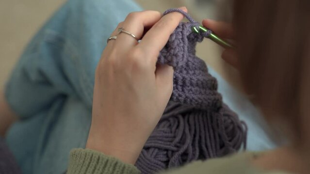 Young woman knits home clothes from woolen threads by crochet. Creation of handmade accessories and clothes from natural materials and fabrics. Wool knitting concept. 4k footage