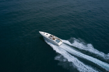 Big high speed white boat with a man at high speed top view. Open white boat fast motion on a dark aerial view.