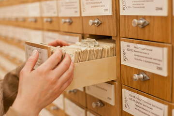 Female student looking for a specific book in old library card catalogue system. Woman browsing through retro style library book collection. Female higher education university or at public library